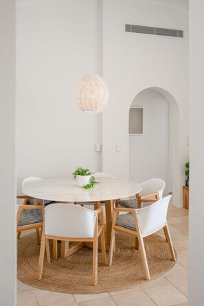 A dining area with a round table, white chairs, a woven pendant light, and a small plant on the table.