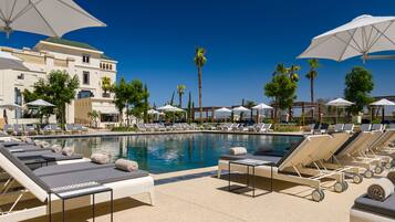 A poolside area with lounge chairs and umbrellas, a clear blue sky, and palm trees.