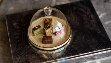 A dessert display with various sweets under a glass dome, placed on a book with visible text.