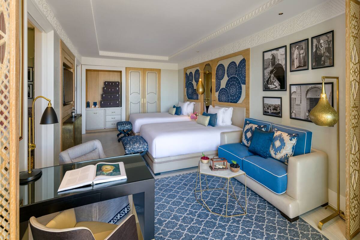 Une chambre d’hôtel avec un grand lit, un canapé bleu, un bureau avec une lampe et un tapis à motifs.