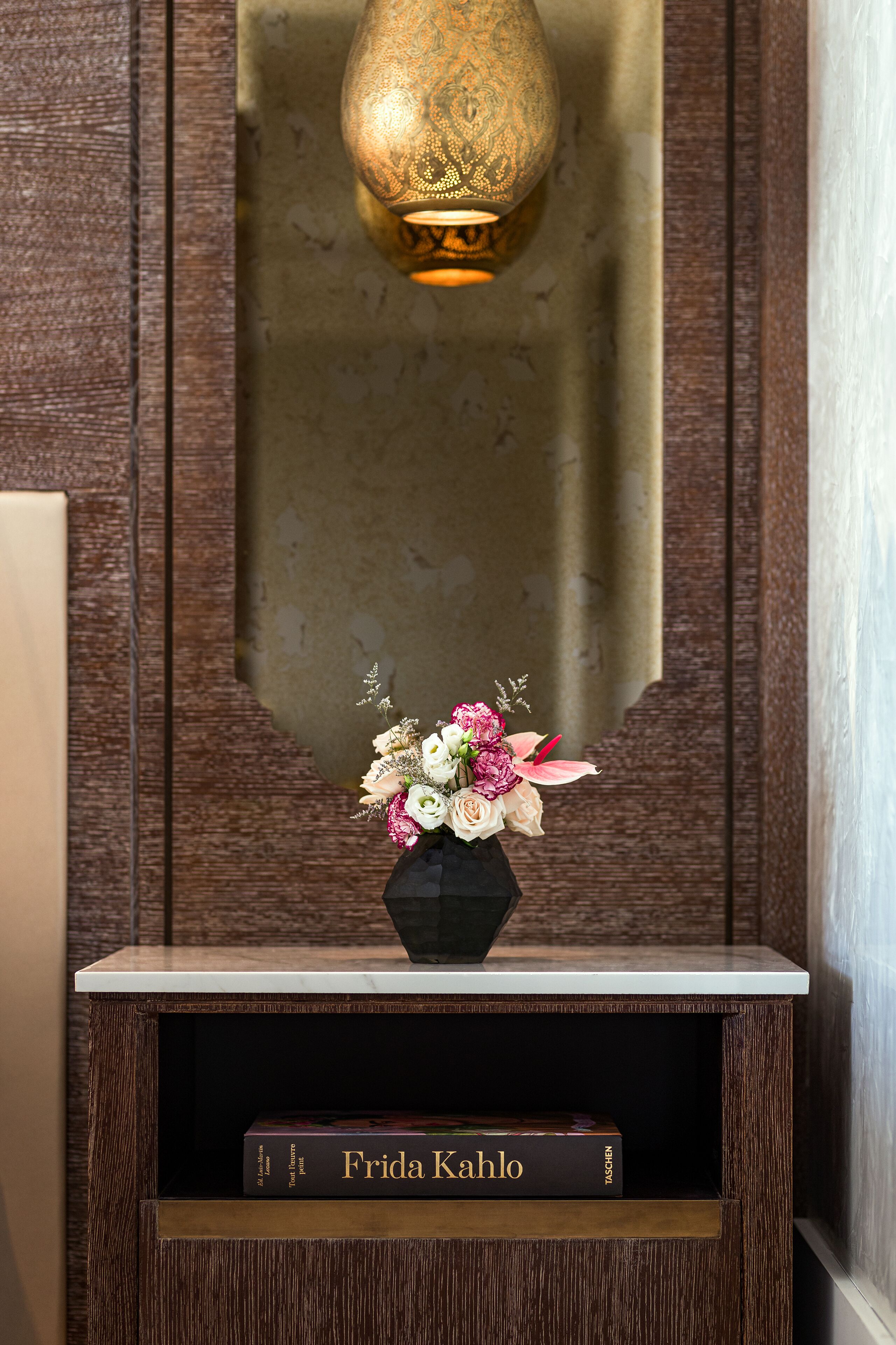 A wooden console table with a vase of flowers and a book titled "Frida Kahlo" on it.