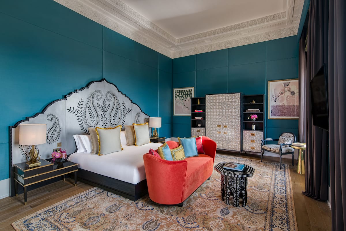 Une chambre à coucher avec un grand lit, un canapé rouge, un tapis à motifs et une tête de lit décorative.