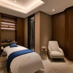 Relax in a serene space with a neatly made bed, a side table, and a comfortable armchair.