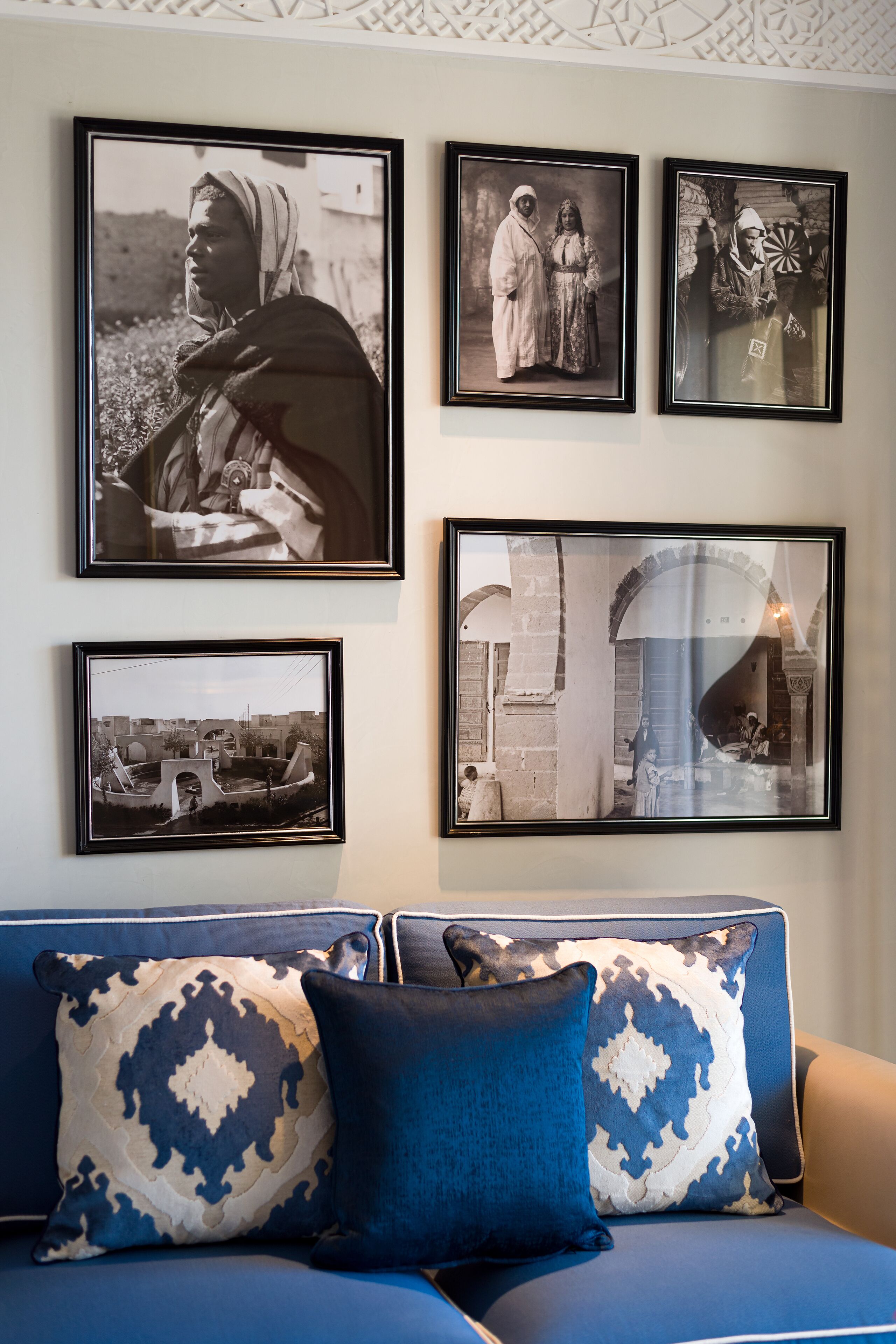 A living room with a blue sofa, patterned cushions, and four framed black-and-white photographs on the wall.