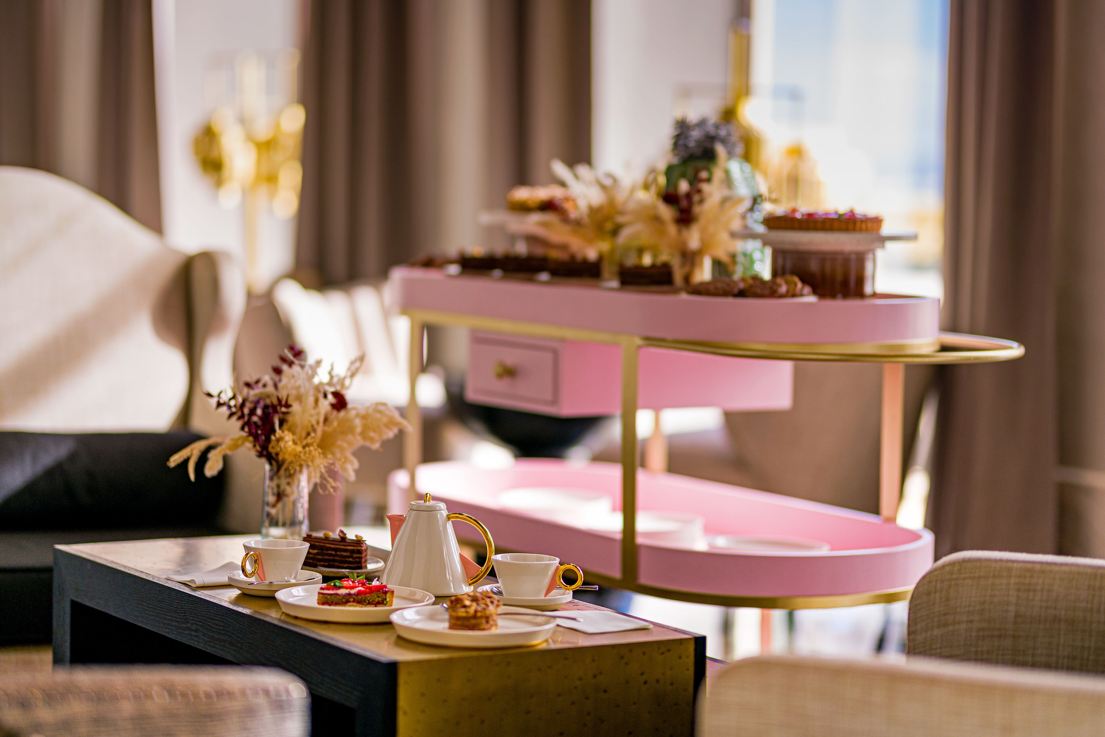 A dining table with a pink and gold tray, a white teapot, and various pastries and desserts.