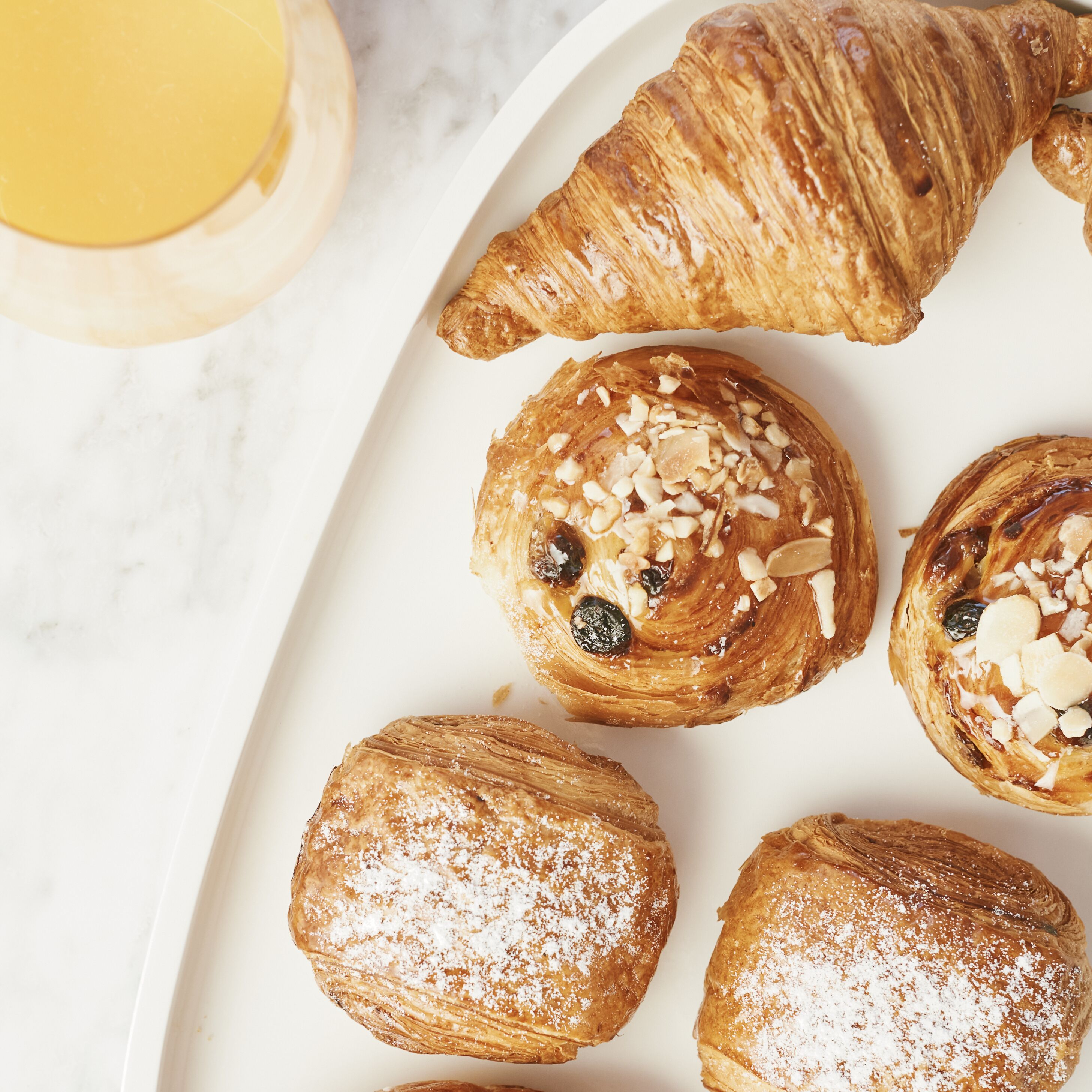 A plate of pastries including croissants and danishes, some with nuts and dried fruit, on a white plate.