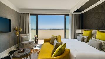 A modern hotel room with a large bed, a sofa, a TV, and a view of the city.