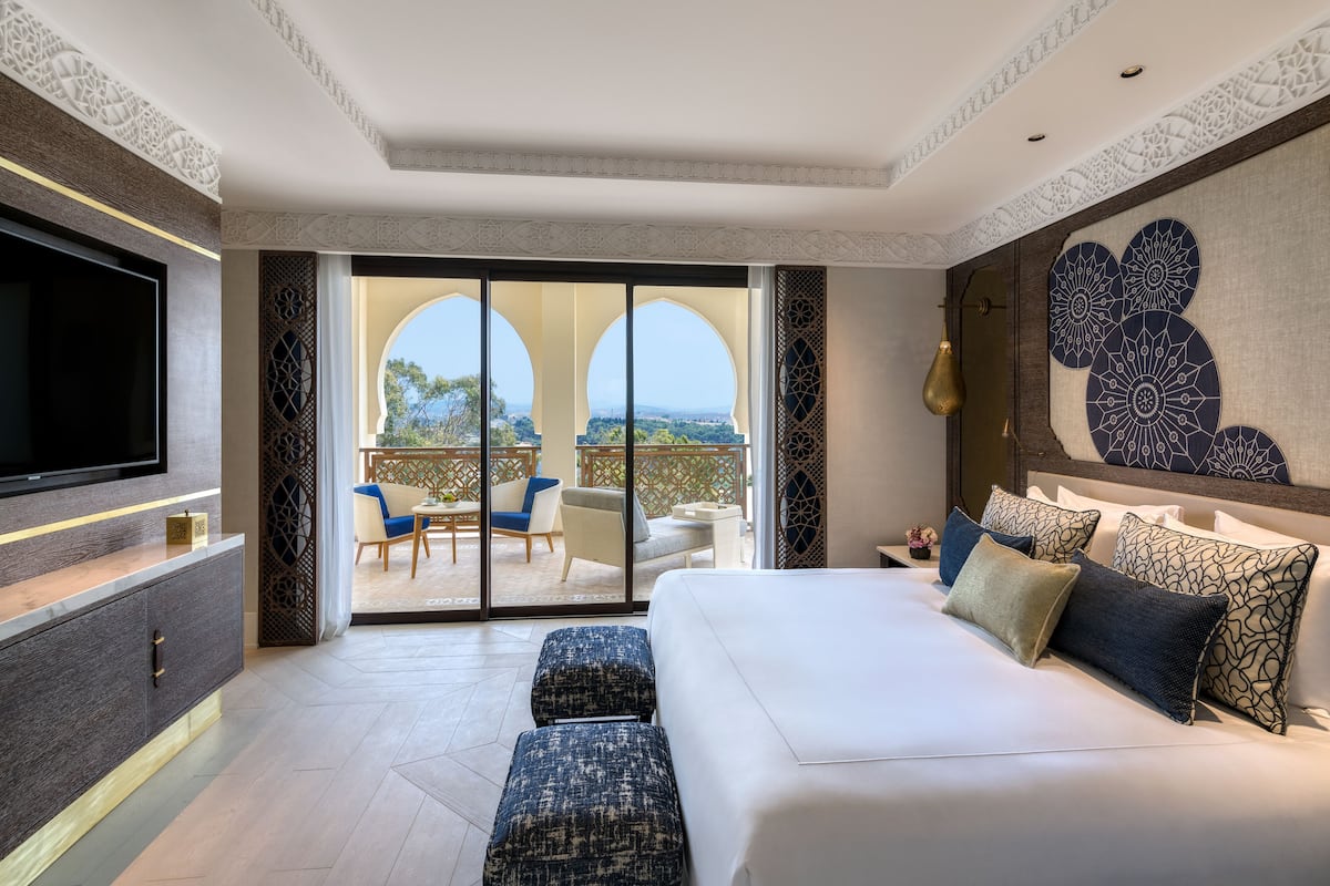 Une chambre d’hôtel moderne dotée d’un grand lit, d’une télévision à écran plat, d’un balcon avec coin salon extérieur et d’œuvres d’art décoratives sur les murs.