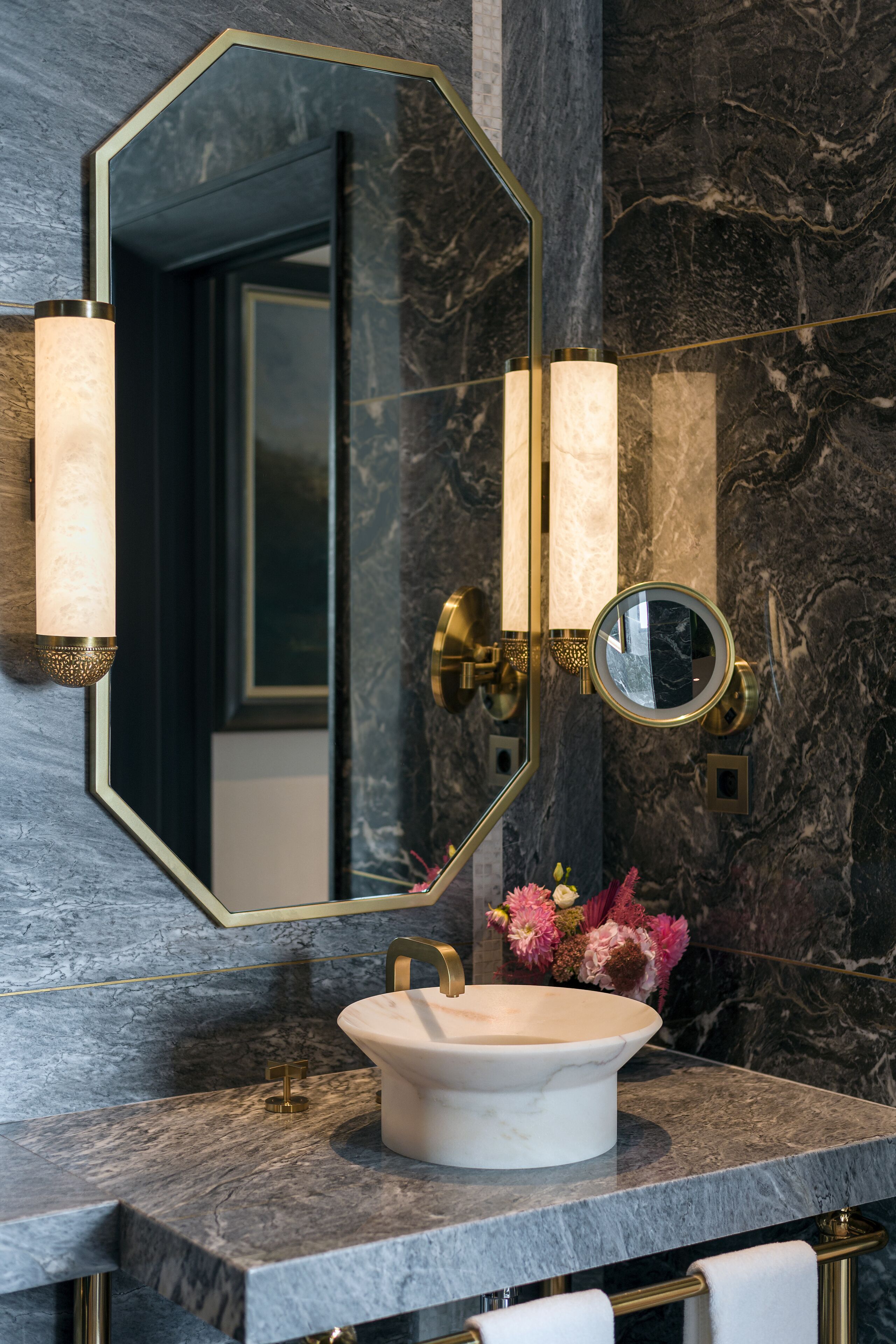 A bathroom with a marble sink, gold fixtures, and a large mirror with a round mirror below it.
