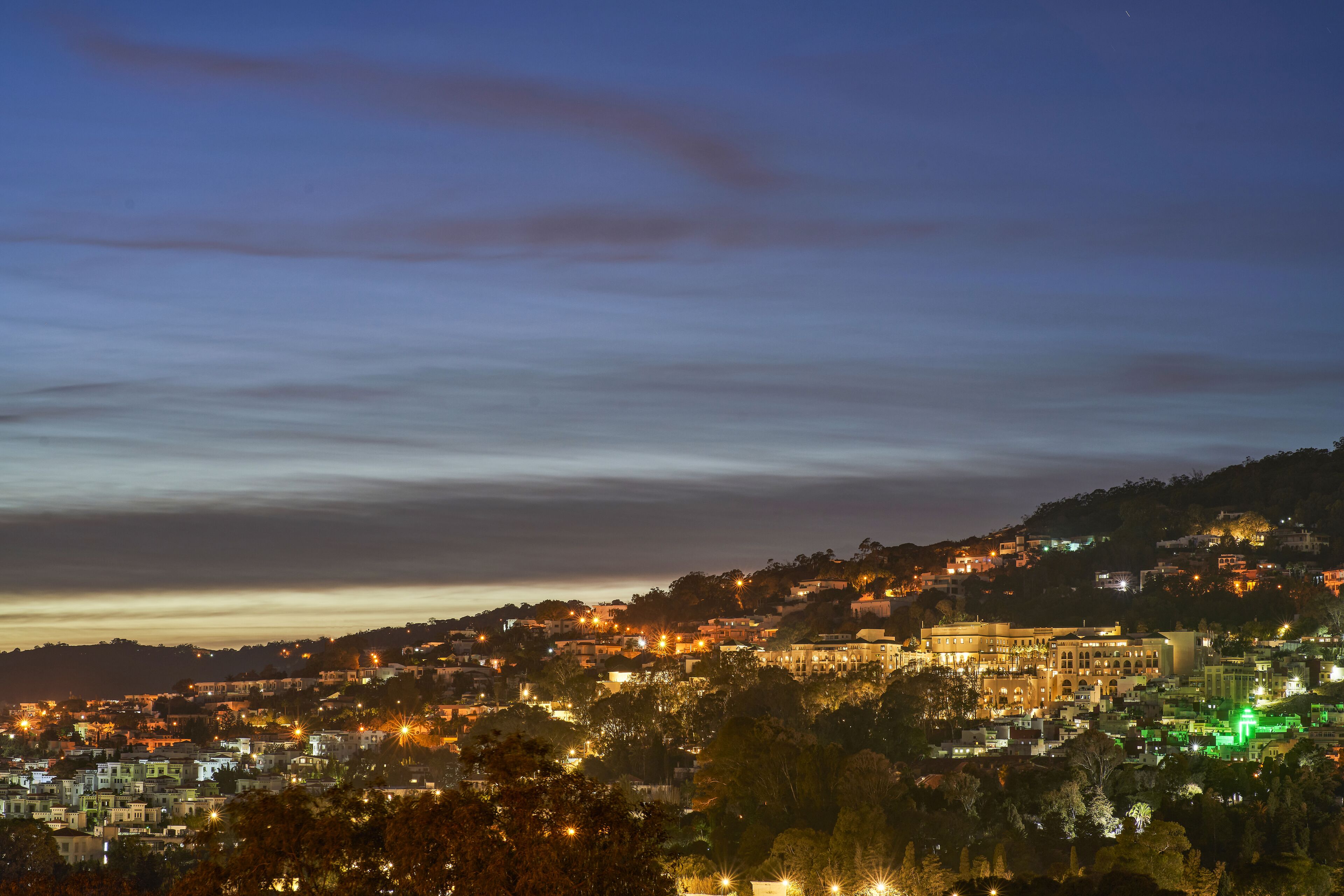 A cityscape at dusk with illuminated buildings and a prominent historical building in the center.