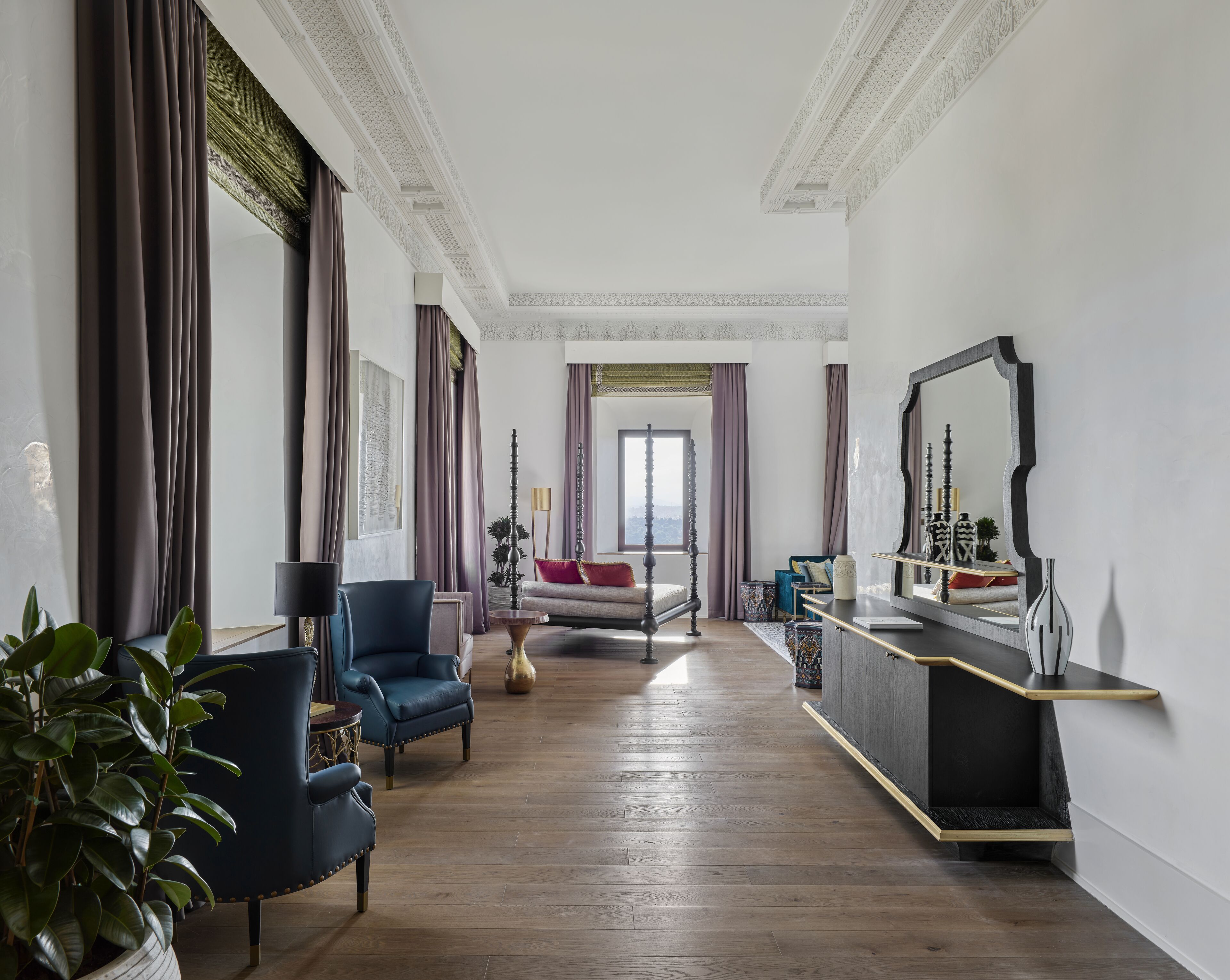 Una habitación amplia con una cama grande, una zona de estar con sofá y sillones, una mesa de comedor y un espejo grande.