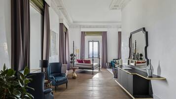 A spacious room with a large bed, a sitting area with a sofa and armchairs, a dining table, and a large mirror.