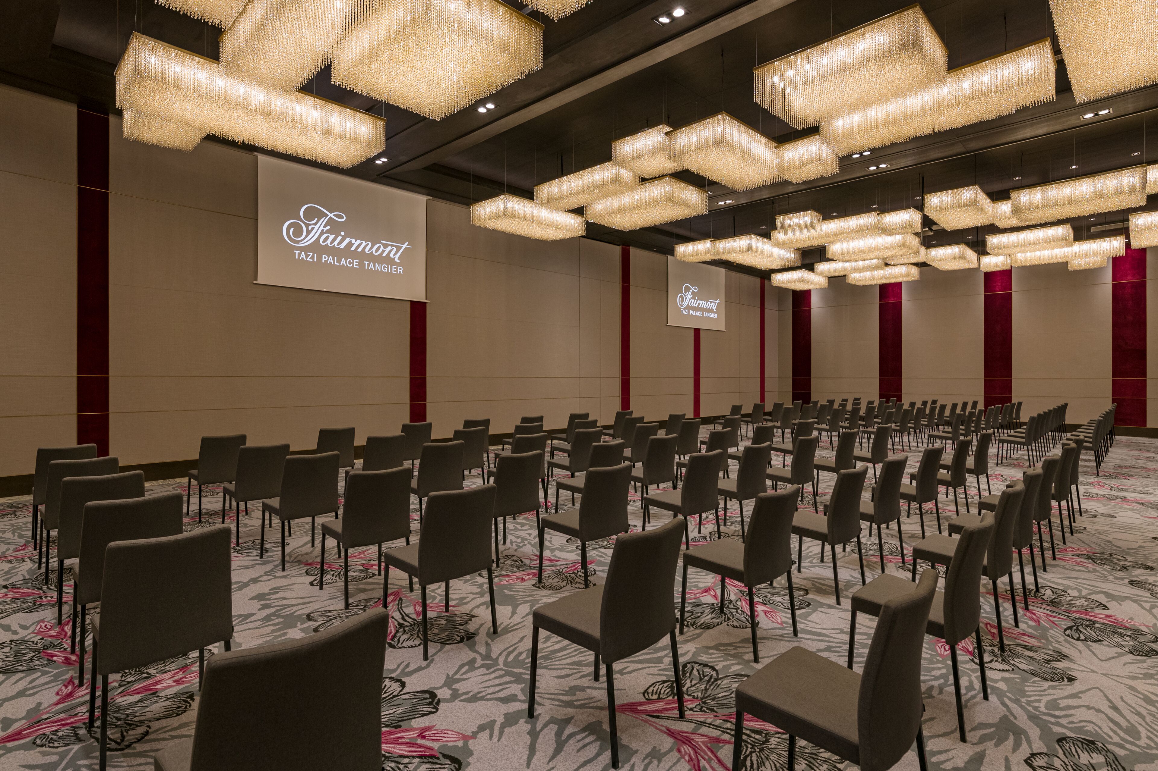 Un salón de conferencias con filas de sillas, candelabros y un cartel que dice "Fairmont TAZI PALACE TANGIER".