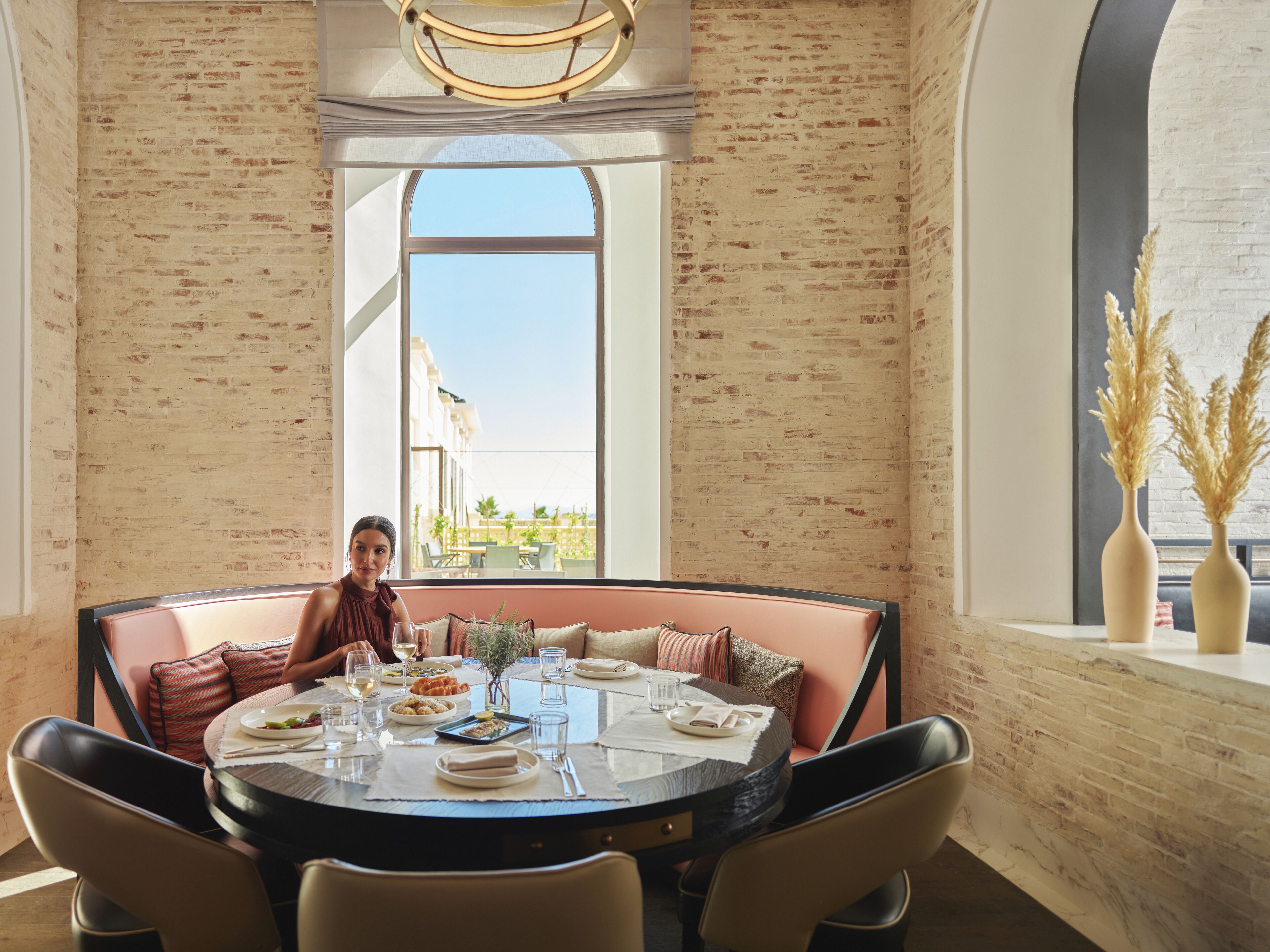 Un comedor con pared de ladrillo, un ventanal y vistas a edificios y zonas verdes.