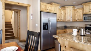 A kitchen with wooden cabinets, a stainless steel refrigerator, granite countertops, a coffee maker, and a dining area with a table and chairs. - Peaceful 3BR - 20mins from Resort + Stunning Grand Teton Views! (Tetonia)