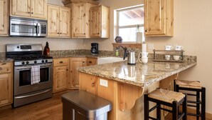 A kitchen with wooden cabinets, a stainless steel stove, granite countertops, and a window with a plant. - Peaceful 3BR - 20mins from Resort + Stunning Grand Teton Views! (Tetonia)