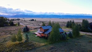 A large house with a red roof and a porch, surrounded by trees and a field. - Peaceful 3BR - 20mins from Resort + Stunning Grand Teton Views! (Tetonia)
