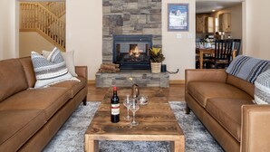 A living room with two brown leather sofas, a stone fireplace, and a wooden coffee table with a bottle of wine and glasses. - Peaceful 3BR - 20mins from Resort + Stunning Grand Teton Views! (Tetonia)