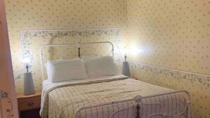 Een enkel bed met een metalen frame, een nachtkastje met een lamp, en behang met een patroon.