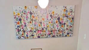 En matplats med ett mörkt träbord och svarta stolar, ett blommigt konstverk på väggen och en liten, inramad skylt på bordet.