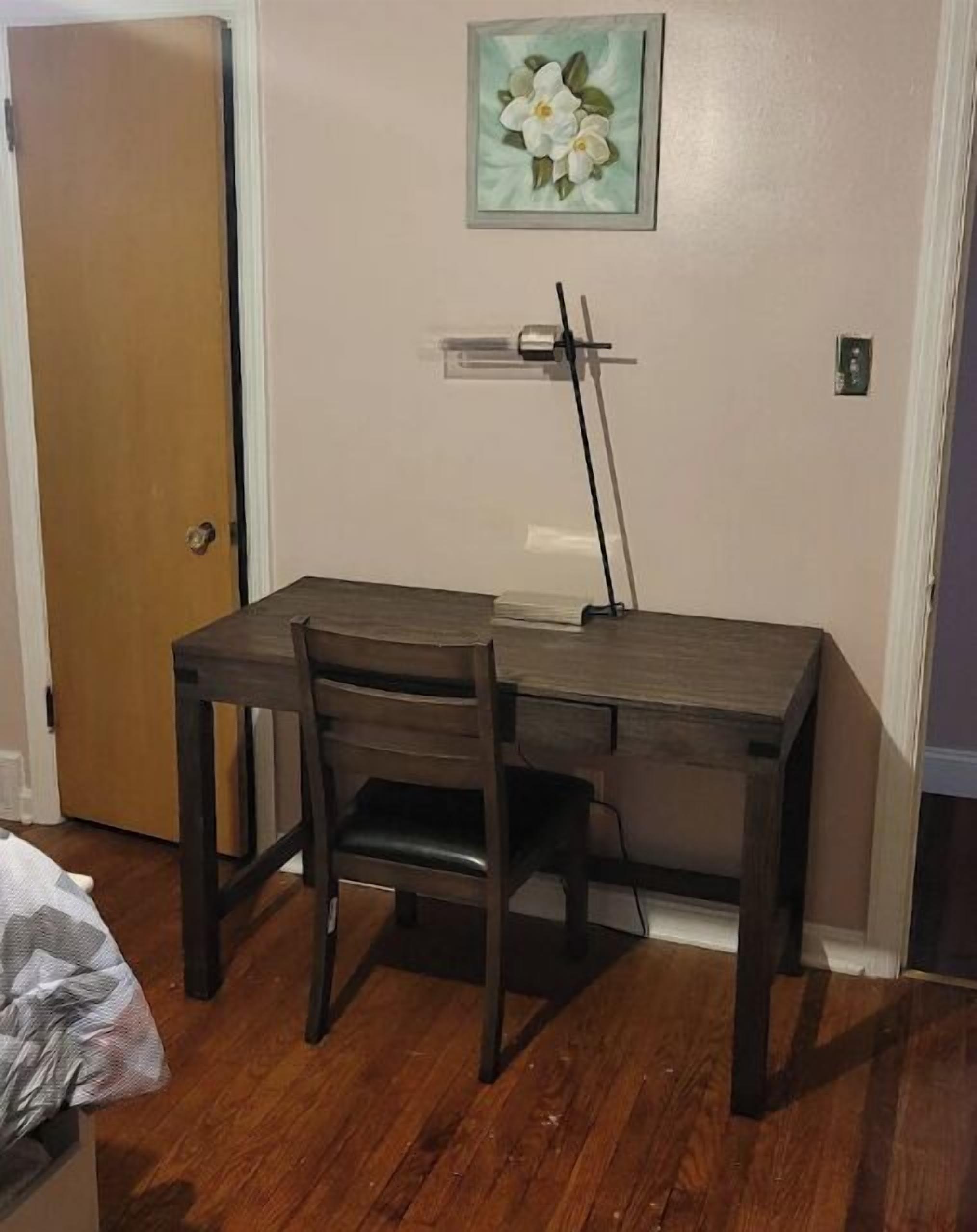 A small room with a wooden desk and two chairs, a door, and a wall-mounted light fixture.