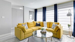 Un salon moderne avec un canapé d’angle jaune, une table basse en verre et un lampadaire.