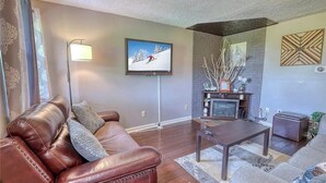 A living room with a brown leather couch, a coffee table, a flat-screen TV, a fireplace, and a patterned rug.