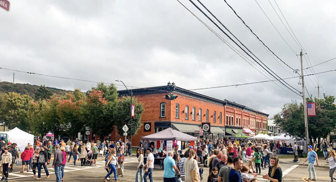 A crowded street scene with a historic brick building, tents, and an American flag.