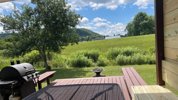 An outdoor patio with a grill, a table, and a view of a grassy field and hills.