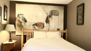 A hotel room with a large abstract painting on the wall, a wooden bed frame, and a bedside table with a lamp.