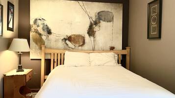 Une chambre d’hôtel avec un grand tableau abstrait au mur, un cadre de lit en bois et une table de chevet avec une lampe.