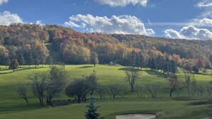 A golf course with a clear sky, autumn-colored trees, and a distant hill.