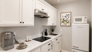A modern kitchen with white cabinets, a built-in microwave, a coffee maker, and a sink.