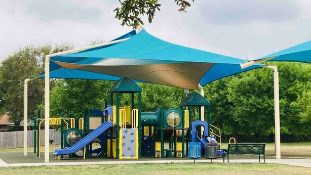 A playground with a blue canopy, play structures, and a bench.