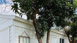 A white mobile home with two wooden chairs and a small table outside, surrounded by a concrete pathway and greenery.