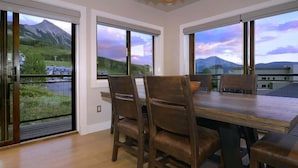 Un comedor con mesa y sillas de madera, ventanas amplias con vista a la montaña y un balcón con barandilla.