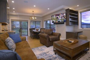 A living room with a sofa, armchair, coffee table, TV, dining area, and a balcony with large windows. - Crested Mtn. North L6 (Crested Butte)