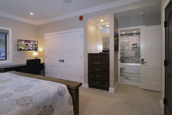 A bedroom with a bed, a TV, a dresser, and a bathroom with a shower and toilet.