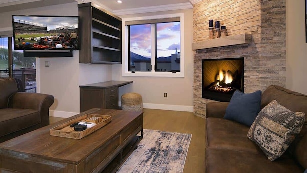 Una sala de estar con chimenea, televisor montado en la pared y un gran ventanal.