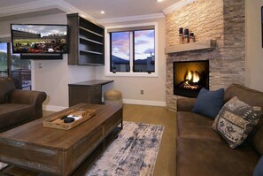 A living room with a fireplace, a television mounted on the wall, and a large window.