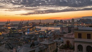 Un paisaje urbano costero al atardecer, con zonas industriales, instalaciones portuarias y edificios históricos.