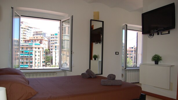 Una habitación de hotel con cama, un ventanal grande, televisión de pantalla plana y una planta en maceta.