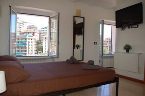 Una habitación de hotel con cama, un ventanal grande, televisión de pantalla plana y una planta en maceta.