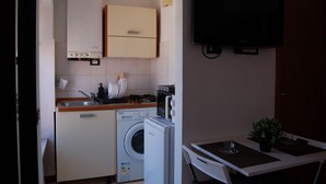 Cocina compacta con lavadora, microondas y una pequeña mesa de comedor con una planta.