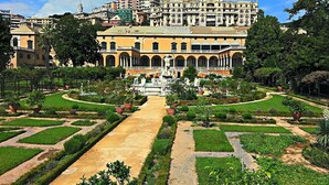 Un edificio grande e histórico con un patio central, rodeado de exuberantes jardines y un cielo despejado.