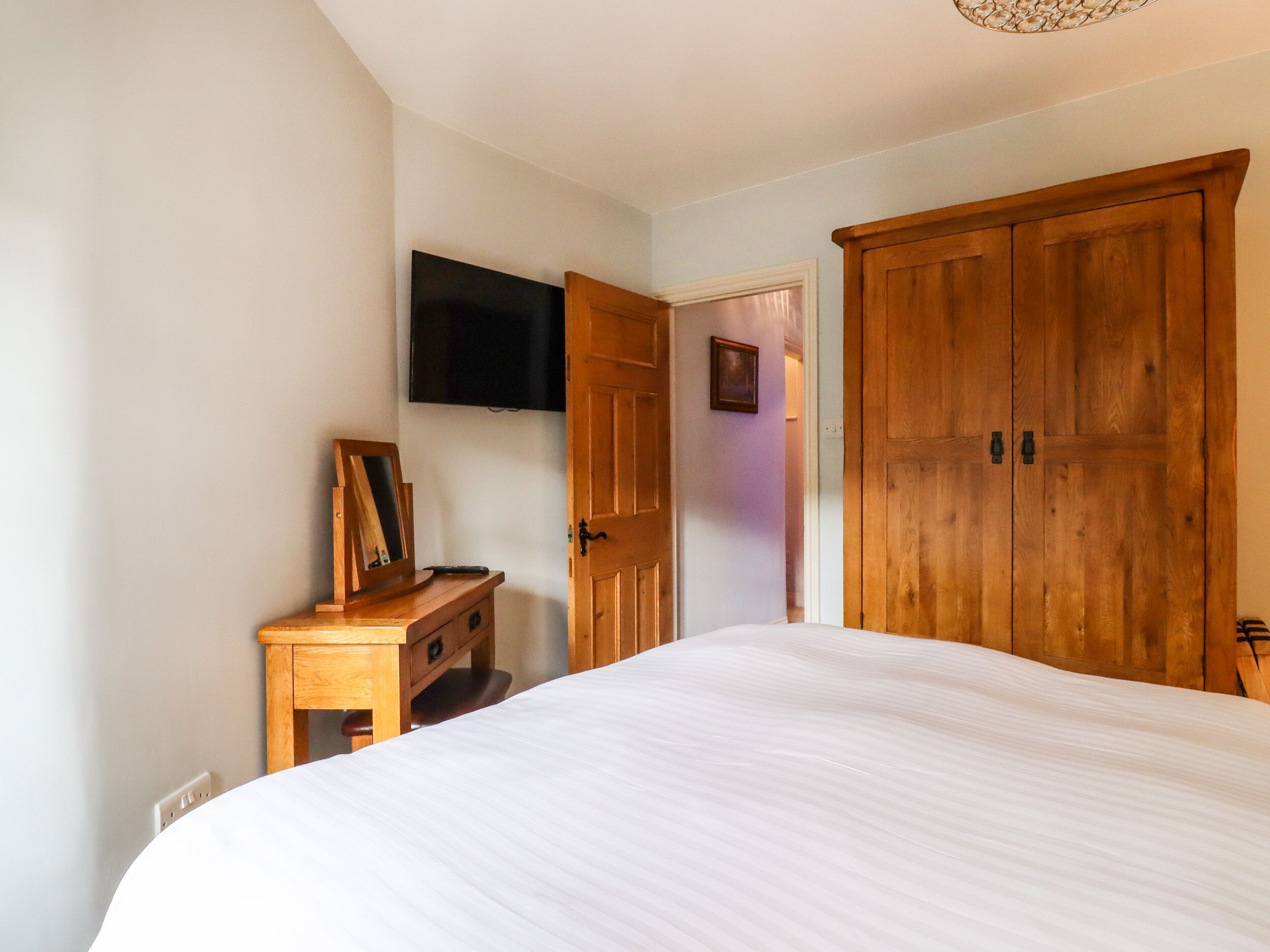 Un dormitorio con una cama grande, un armario de madera, un escritorio con espejo y un televisor montado en la pared.