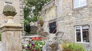 A pig statue with a heart-shaped decoration in front of a stone building with a window. - Squint Cottage (Skipton)