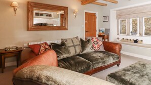 A cozy living room with a leather sofa, a wooden ceiling, a mirror, and a window with a stone wall. - Squint Cottage (Skipton)