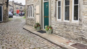 A stone building with a green door, windows, and a cobblestone street. - Squint Cottage (Skipton)