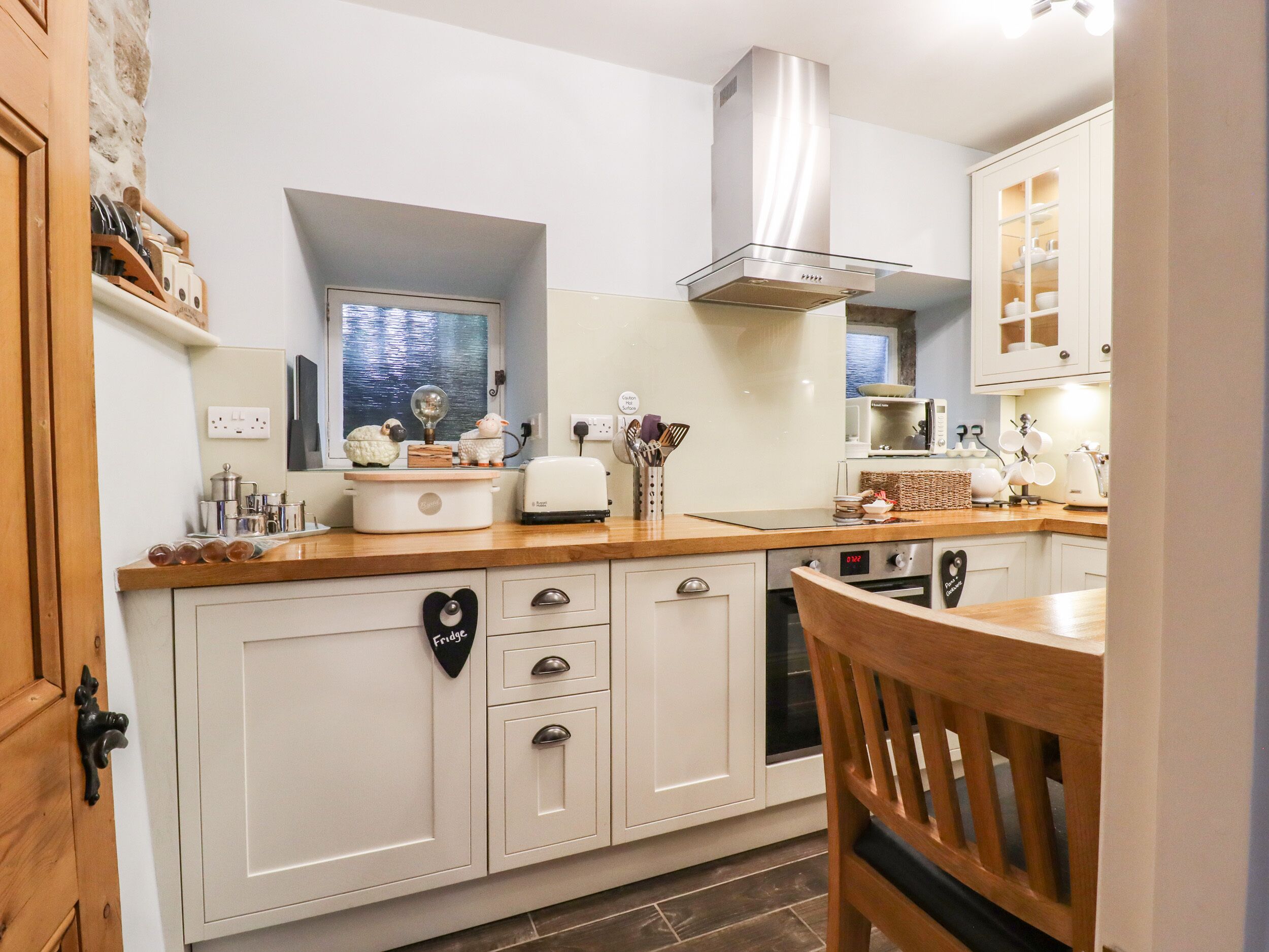 A kitchen with white cabinets, a wooden countertop, a stainless steel range hood, and a microwave.
